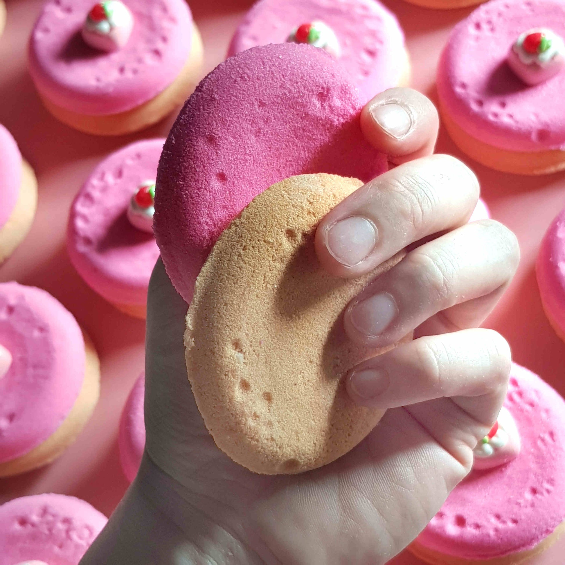pink and beige disc shaped bath bombs with small strawberry dessert charms on top being held in a hand