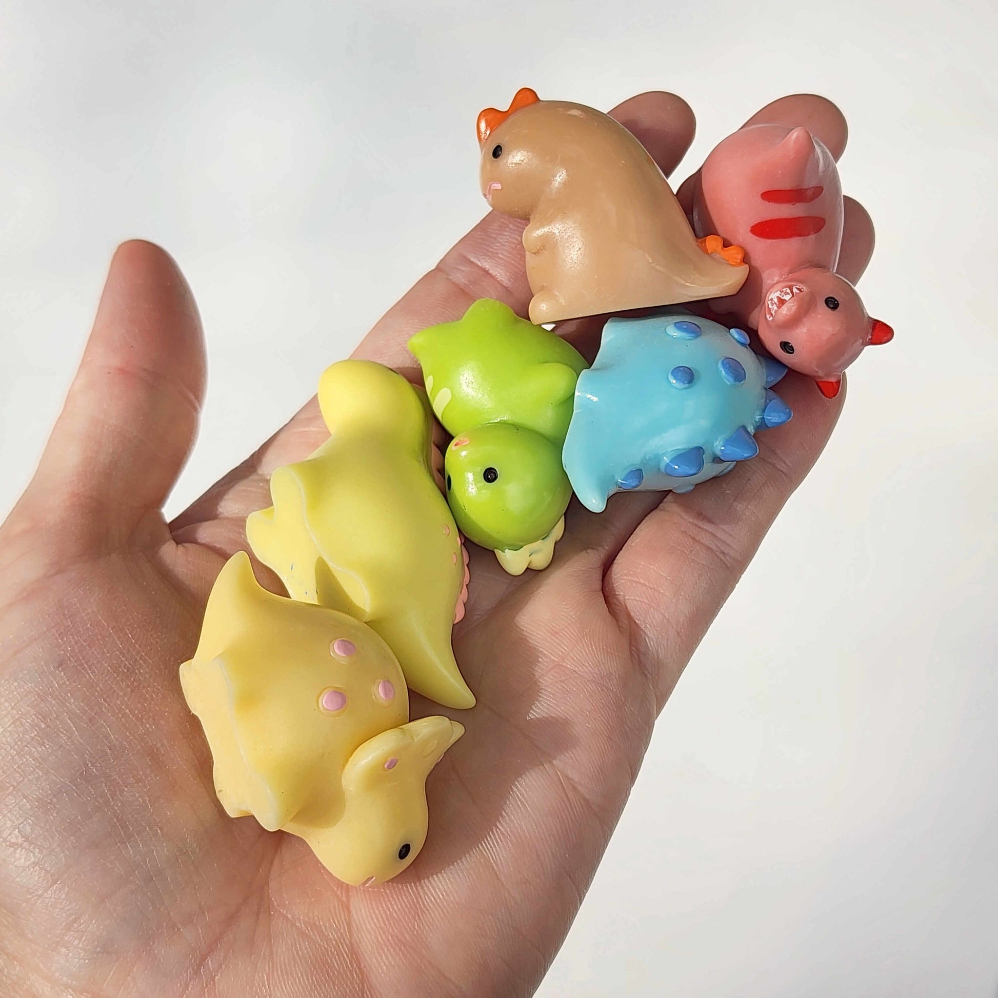 group of colourful round dinosaurs being held in a hand on a white background