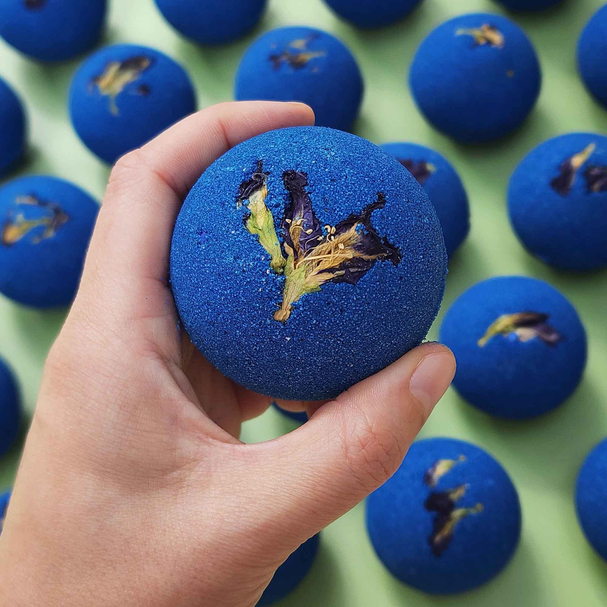 deep blue bath bombs with dried pea flowers on top on a plain green background