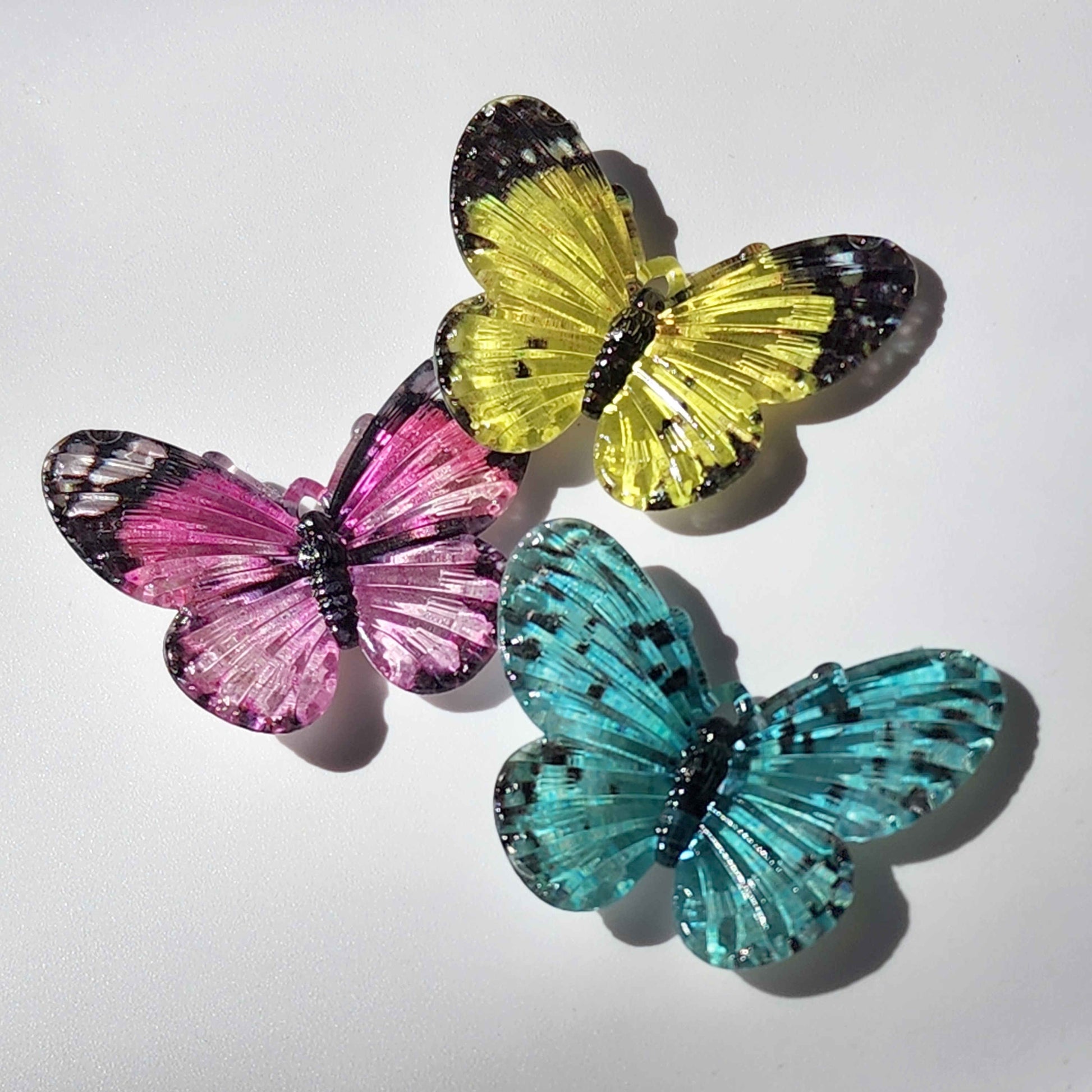three vibrant acrylic butterfly charms on a white background