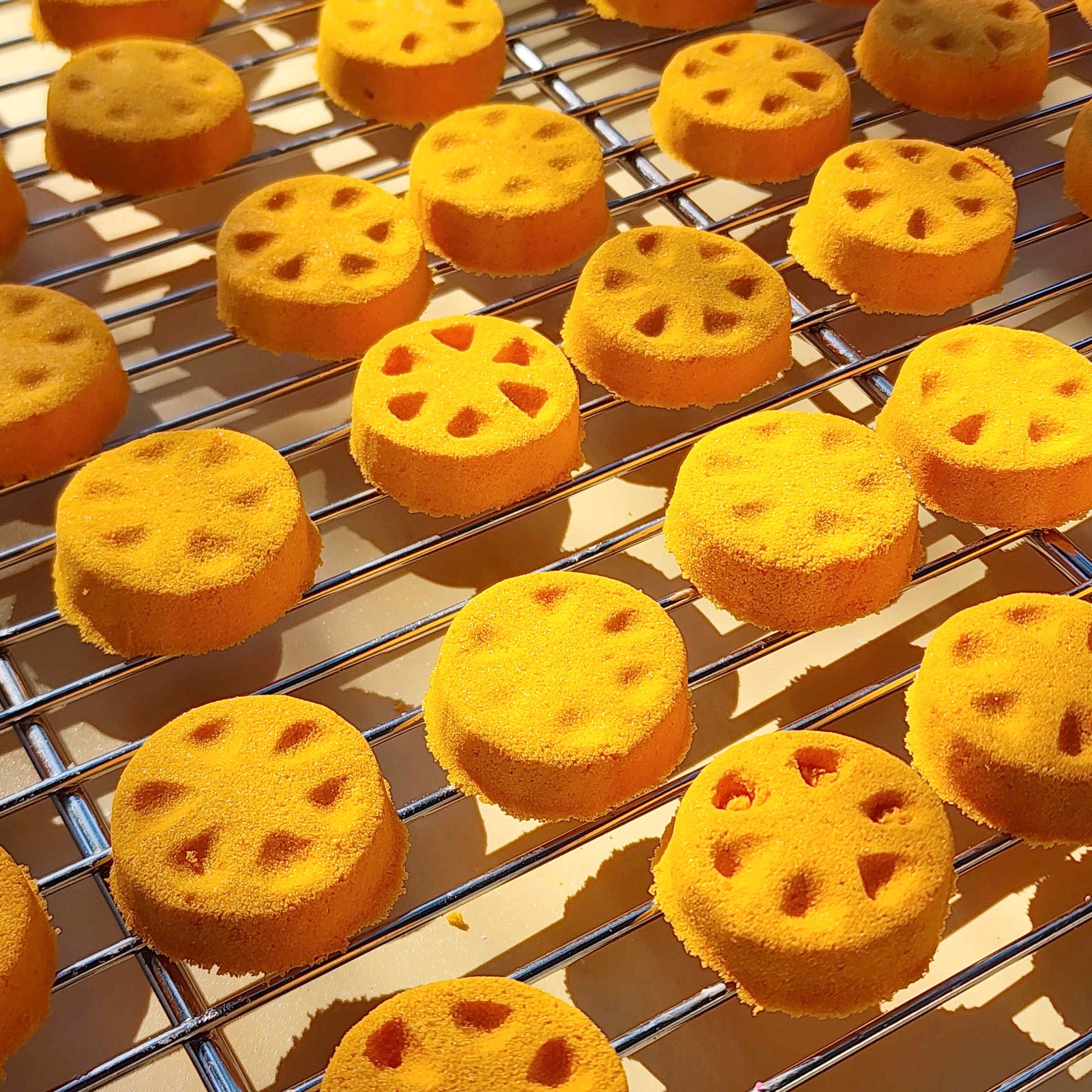 Orange slice shaped mini bath bomb layed out in an array across a plain neutral background