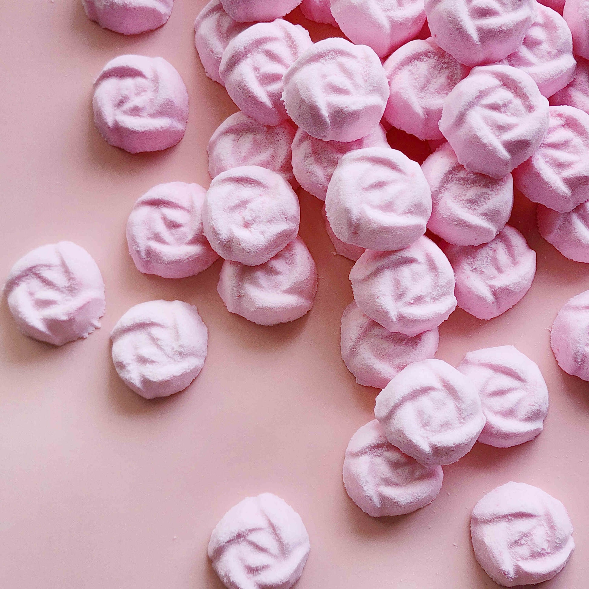 light dusty pink coloured mini bath bombs in the shape of roses laid out neatly on a plain pink background