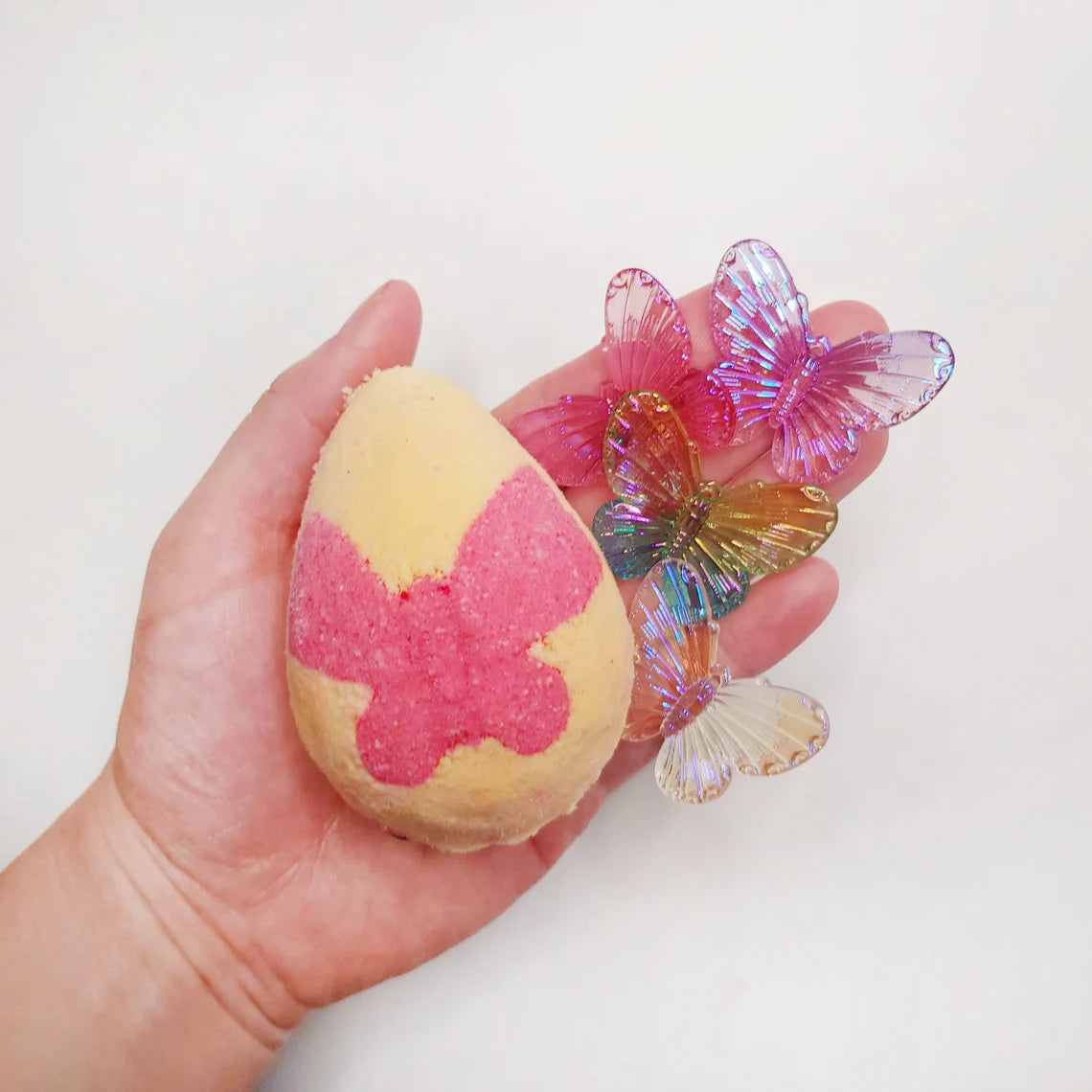 peach egg shaped bath bomb with a bright pink butterfly in the middle being held with vibrant translucent butterfly charms