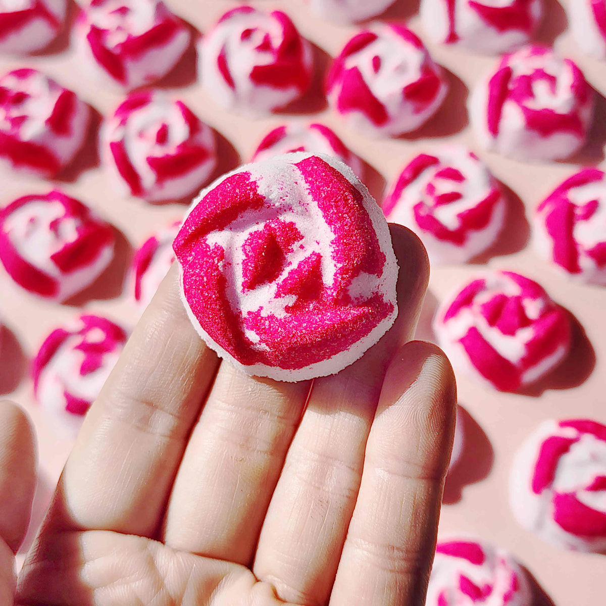 Hand holding a pink and white Peony Rose mini bath bomb