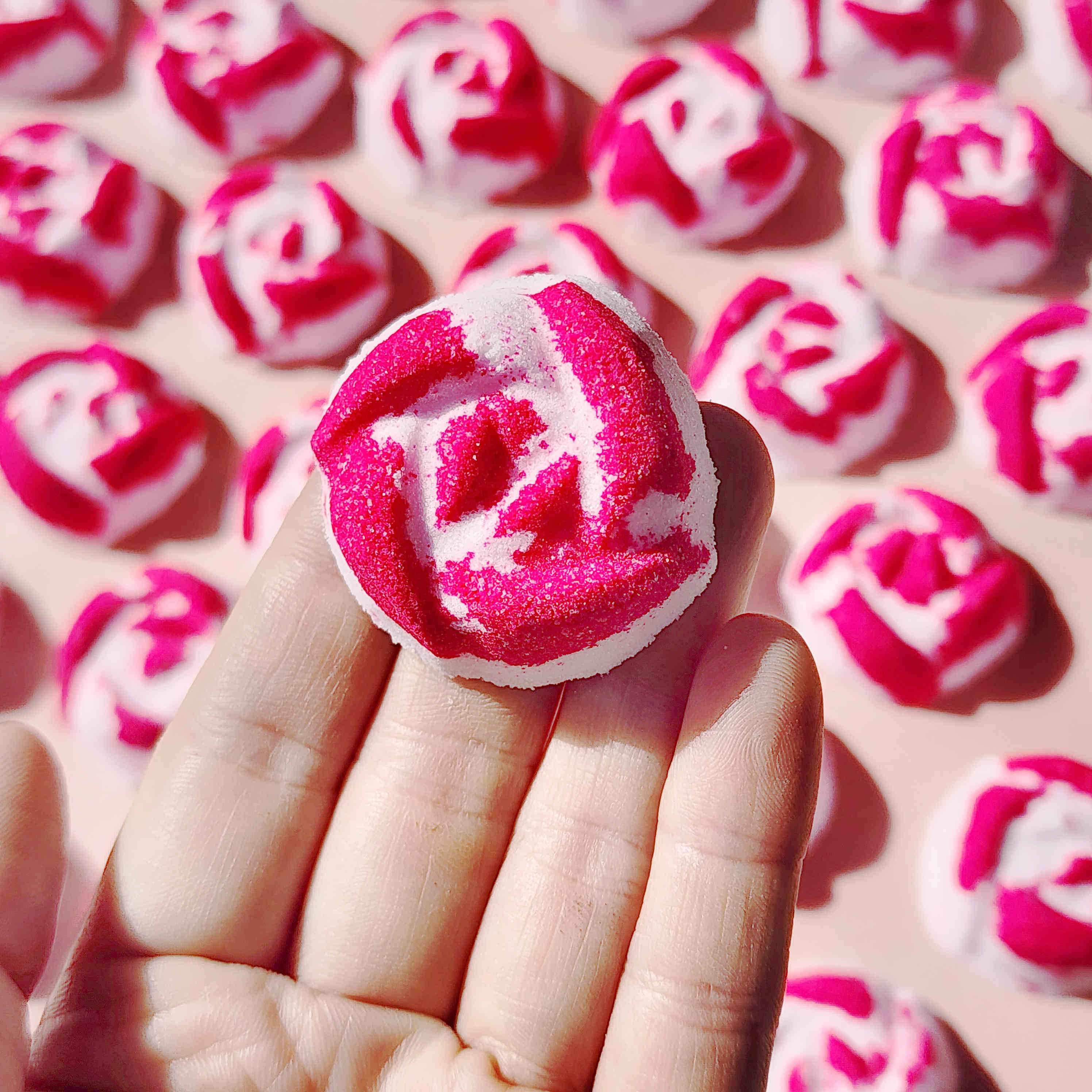 Hand holding a pink and white Peony Rose mini bath bomb