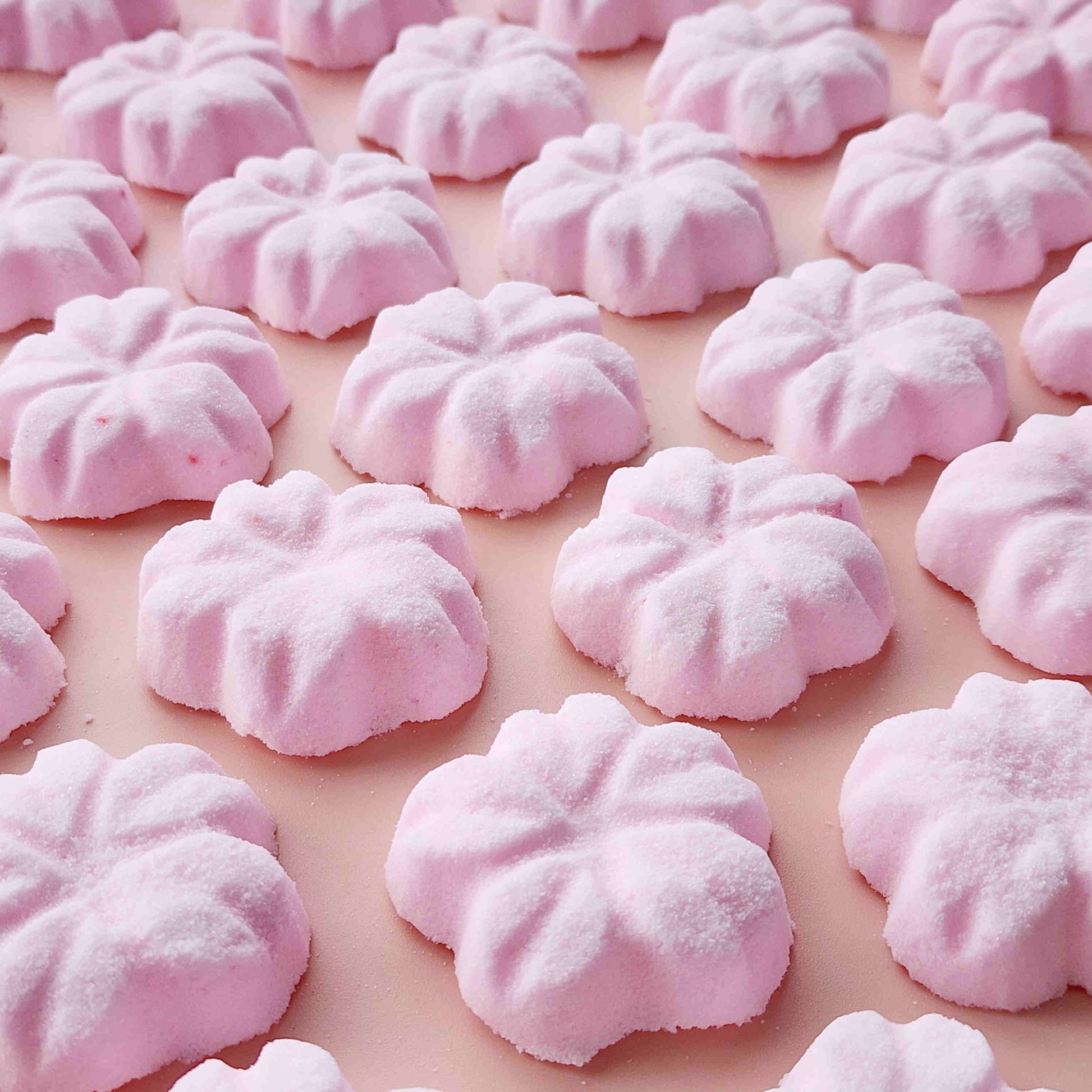 5 petal cherry blossom shaped bath bombs coloured light pink on a plain pink background