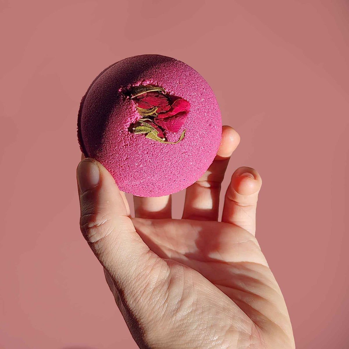 velvet red round aromatherapy bath bombs with dried rose buds on a dusty pink background