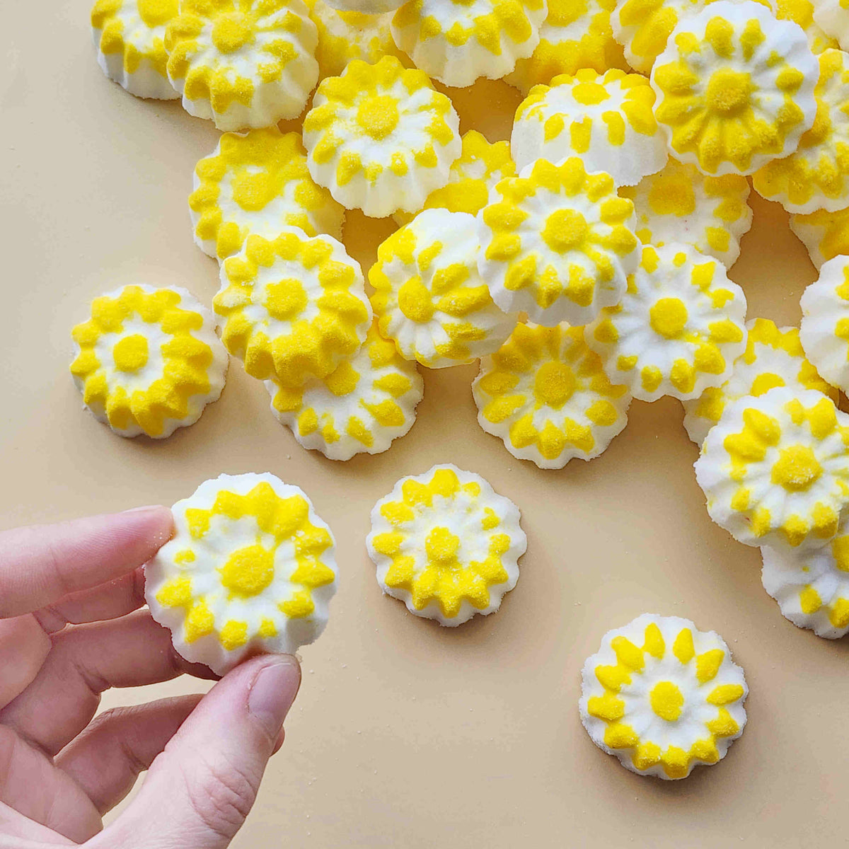 chamomile shaped mini bath bombs with a white base and yellow detail on a neutral plain background