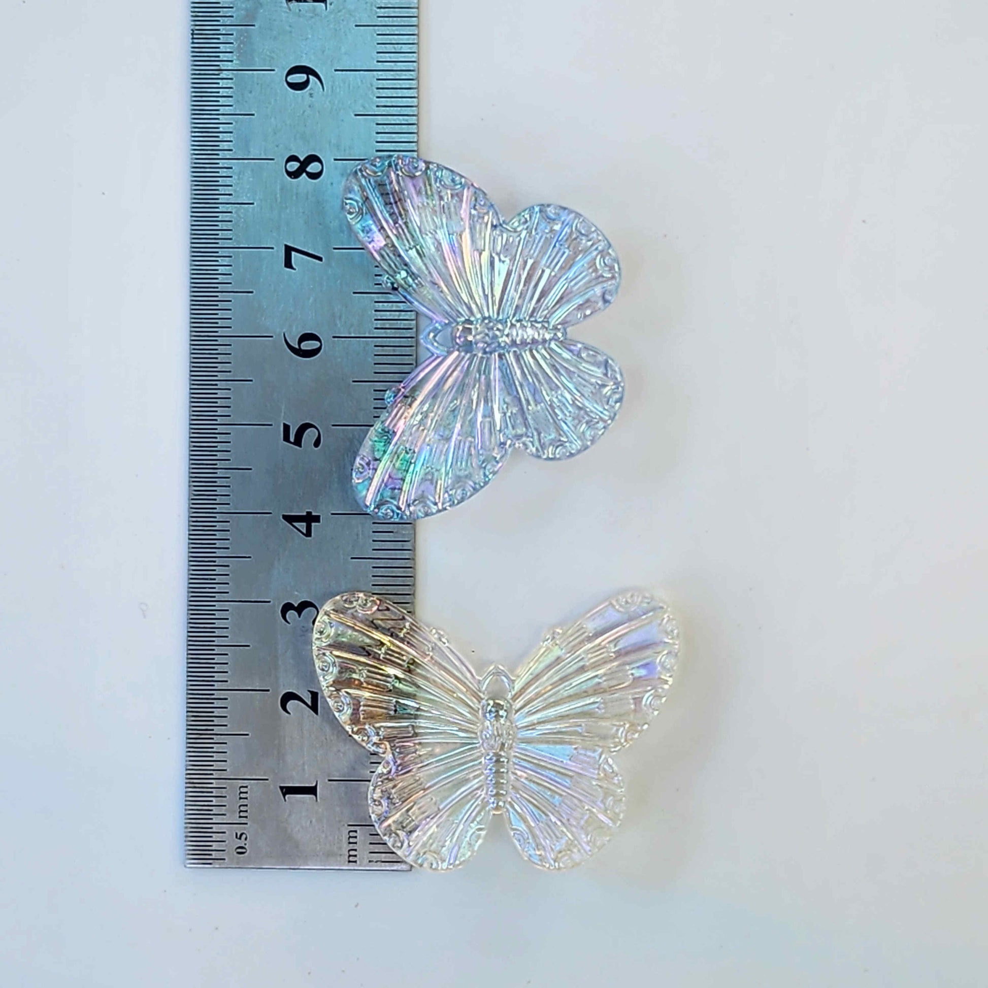 measurements for two clear butterfly charms on a metal ruler on a white background