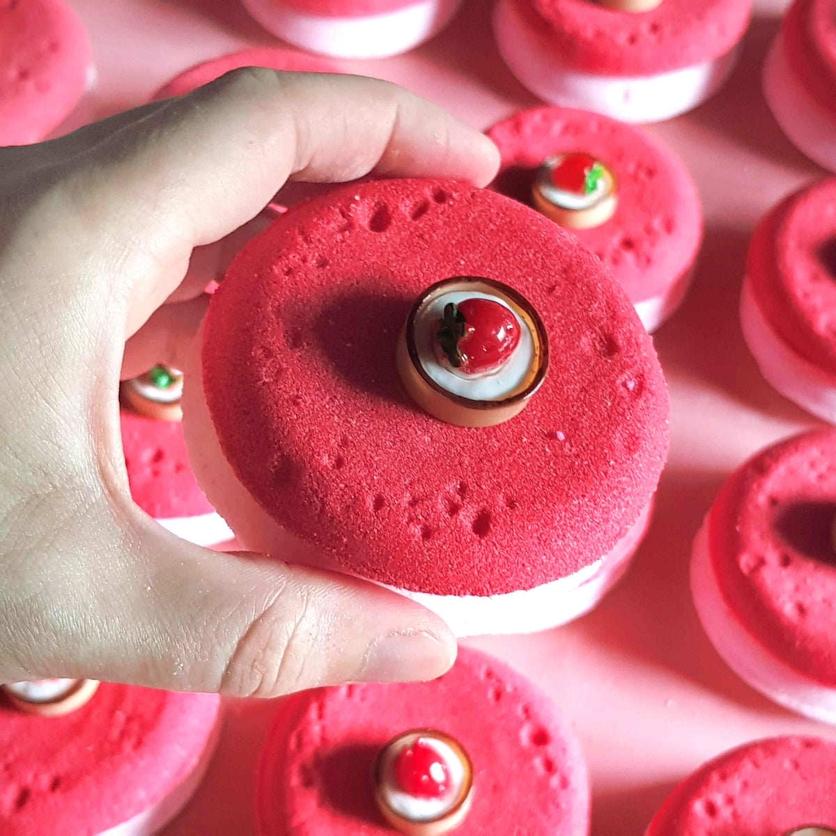 Flat disc shaped bath bombs stacked and placed in a tidy array on a plain pink background with one held in a hand close up