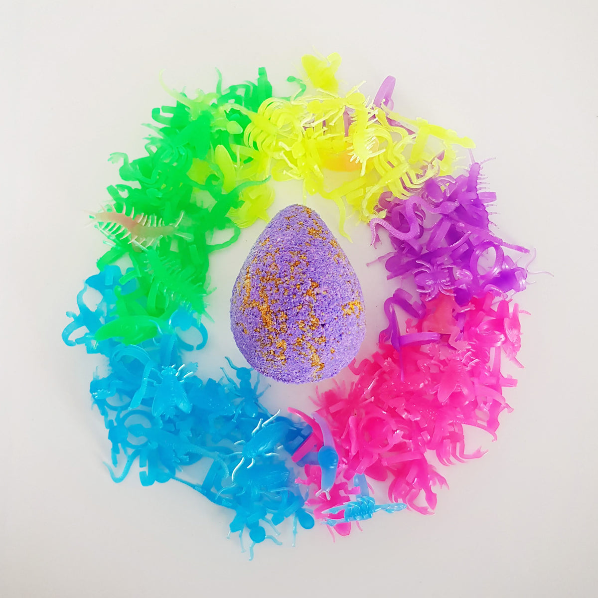 bright purple egg shaped bath bomb surrounded by neon glow in the dark insect themed toy rings