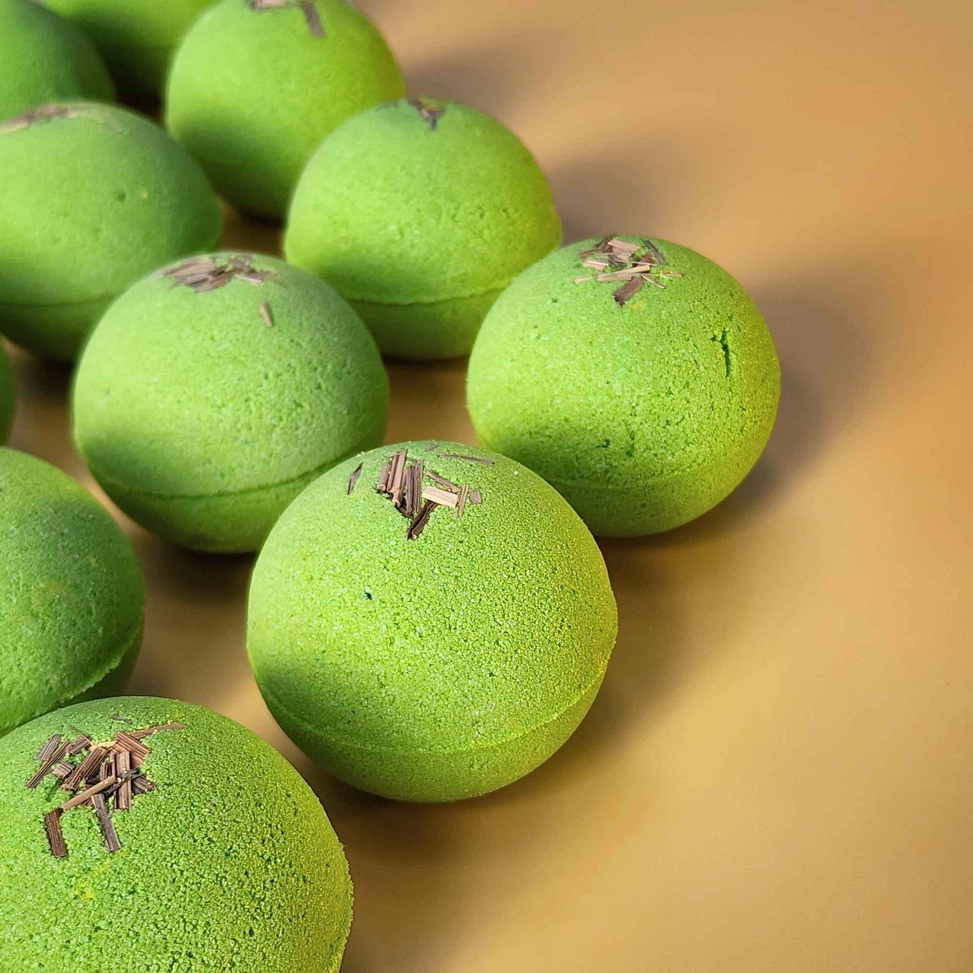 Multiple bright green Repair aromatherapy bath bombs topped with small pieces of dried lemongrass on a warm yellow background