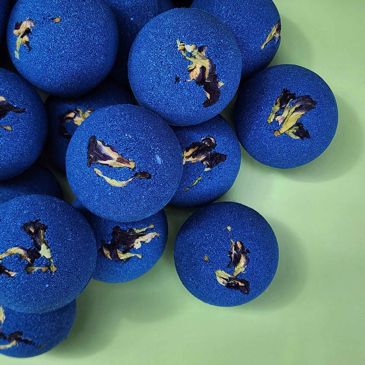 stack of deep blue bath bomb with dried pea flowers on top on a plain green background