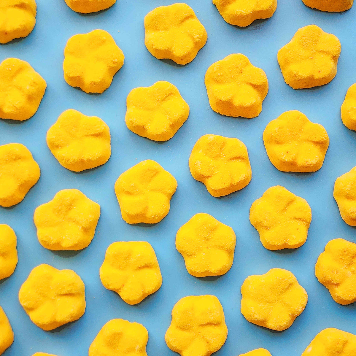 yellow frangipani shaped bath bombs placed in a neat array on a blue background