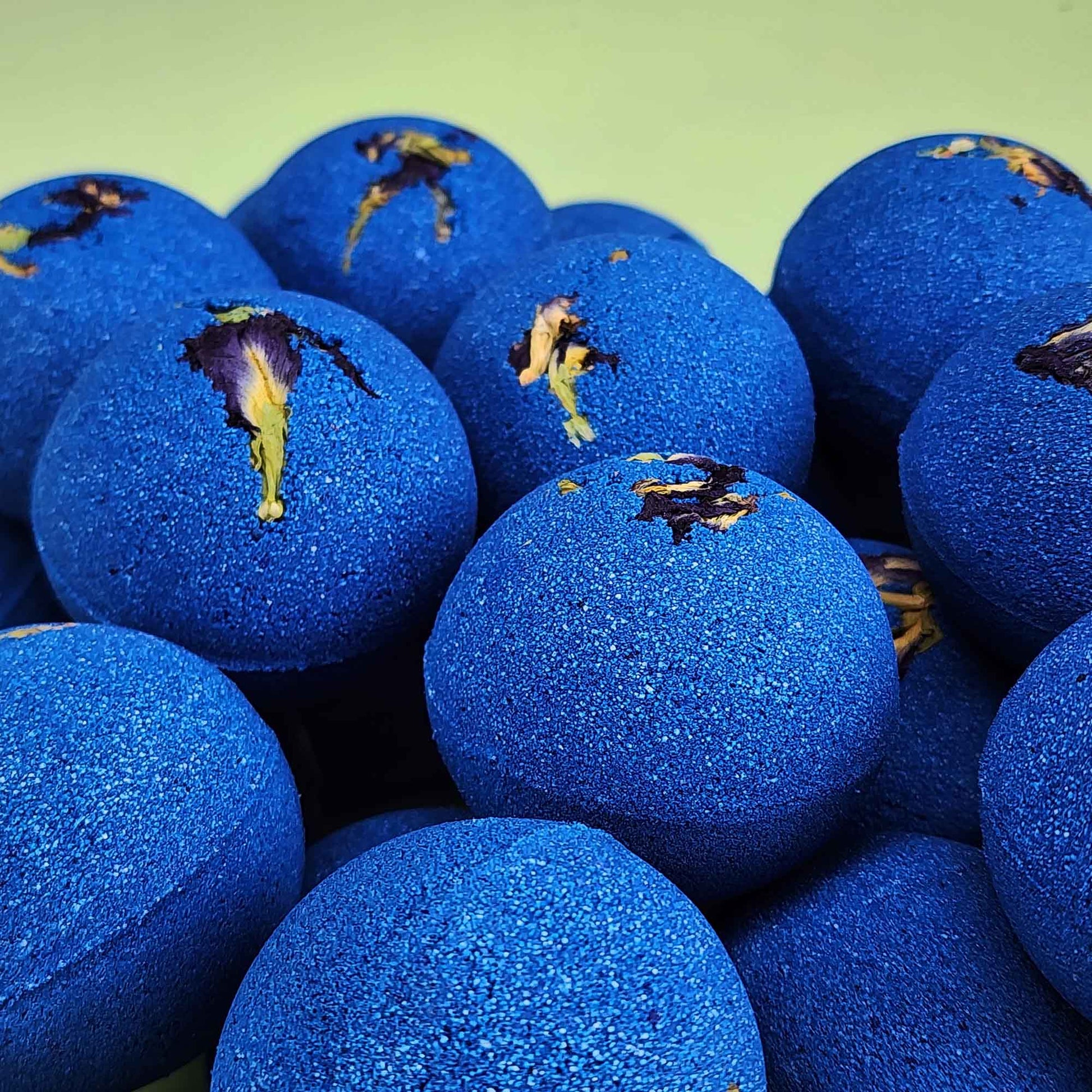 stack of deep blue bath bombs with dried pea flowers on top on a plain green background