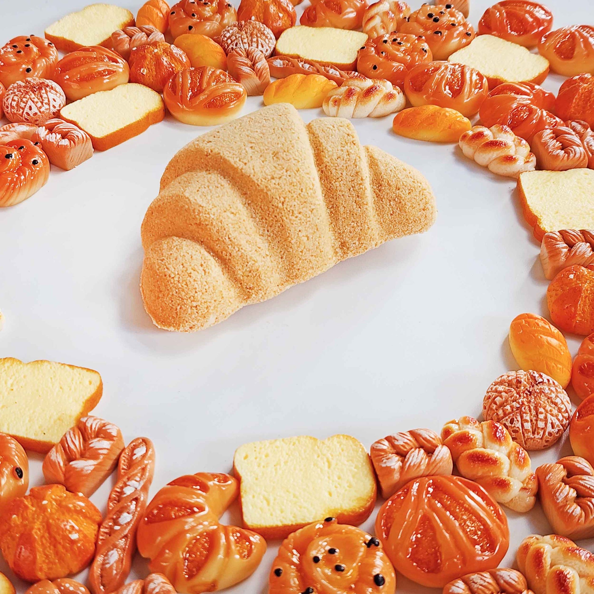 Croissant bath bomb centered among miniature bread-shaped toys