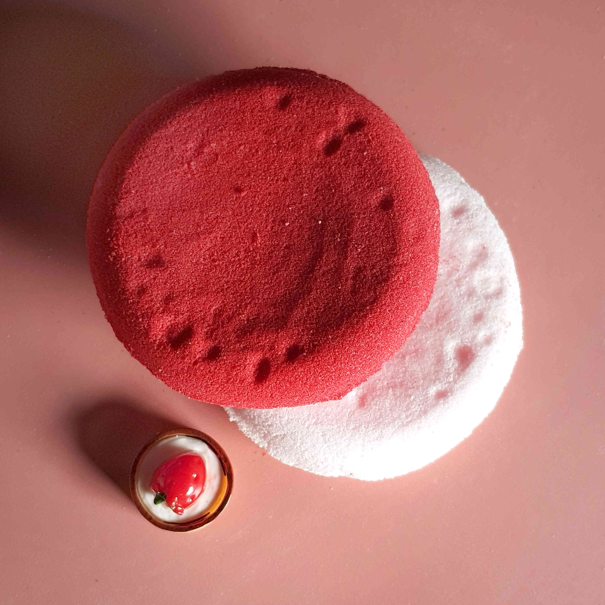 Flat disc shaped bath bomb stacked and placed on a plain pink background