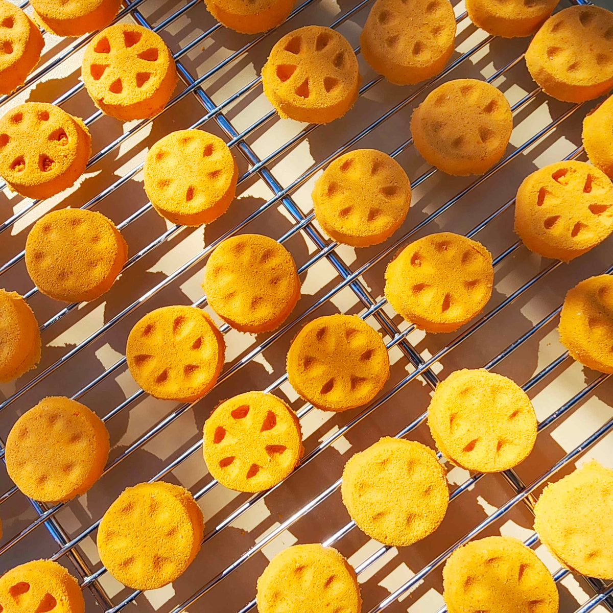 Orange slice shaped mini bath bomb layed out in an array across a plain neutral background