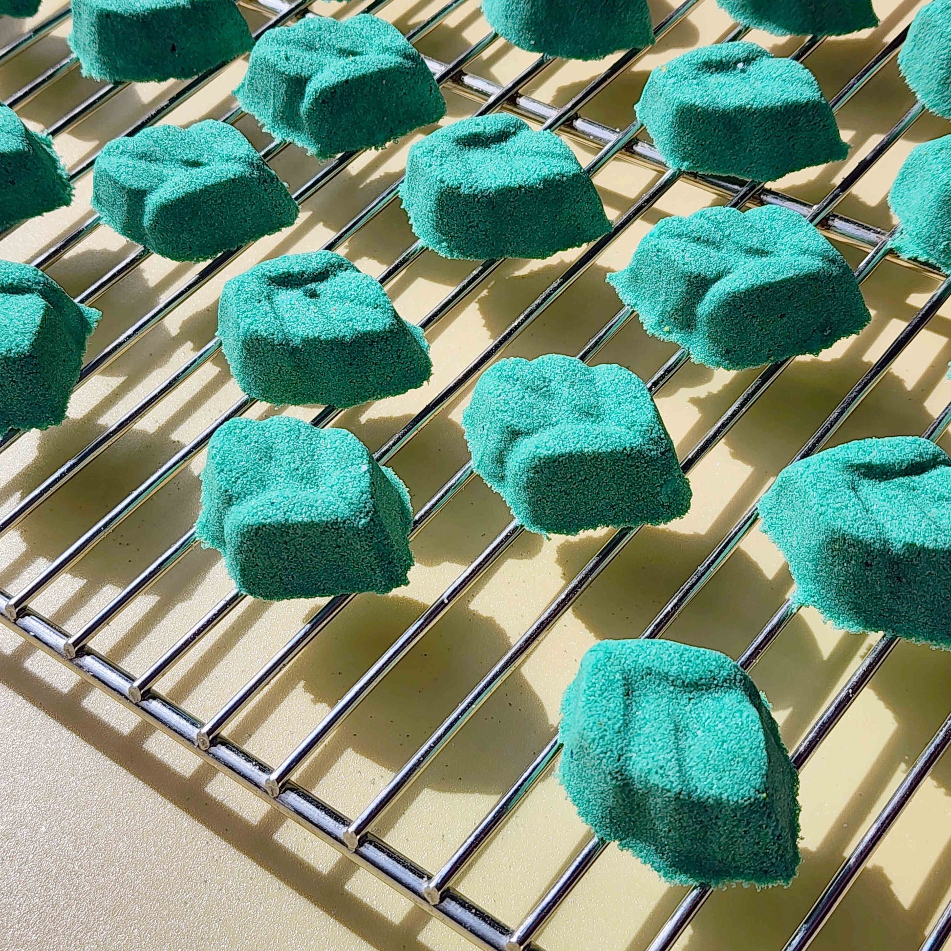 teal leaf shaped mini bath bomb laid out in a neat array over a plain beige background