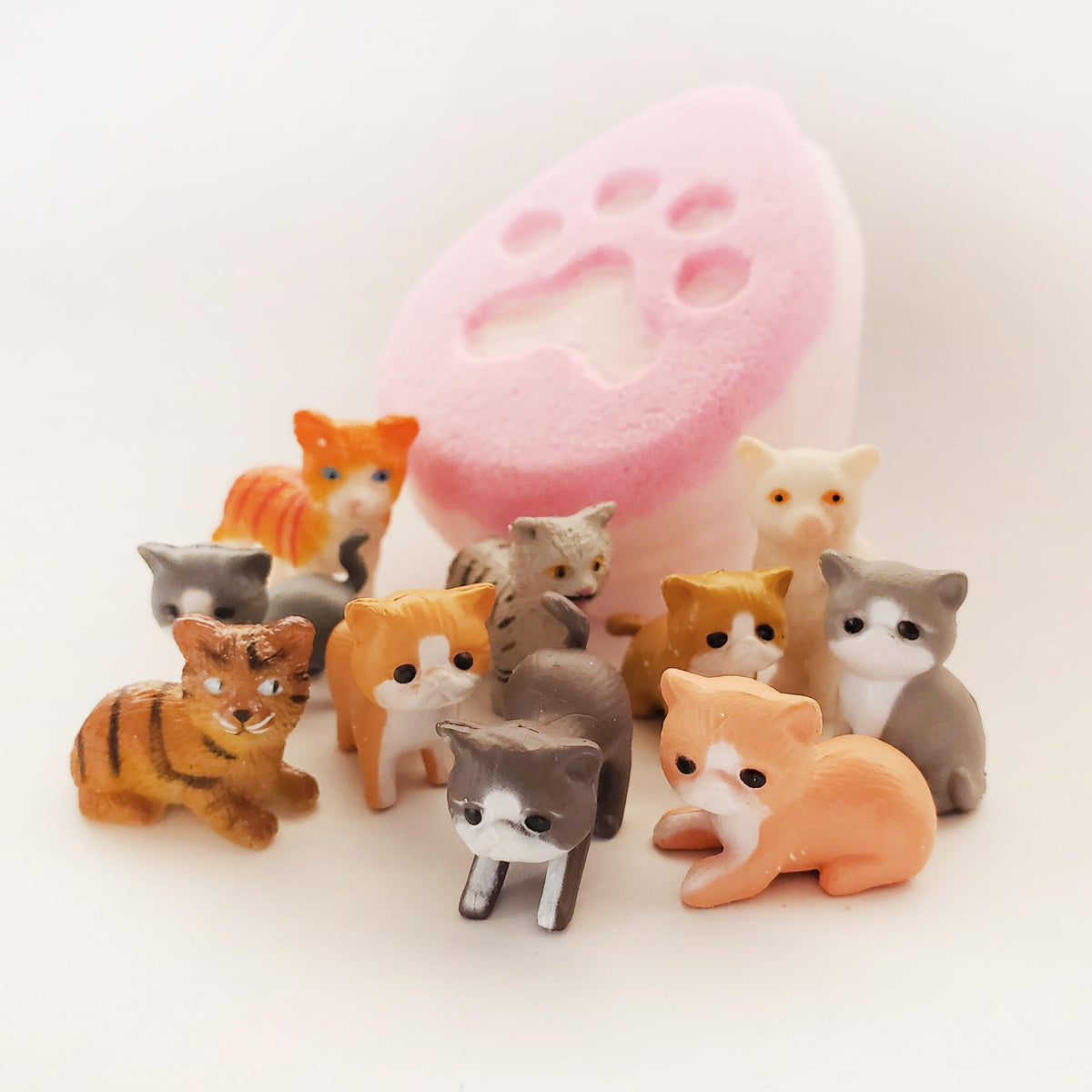 pink fat egg shaped bath bomb with a cat paw print embossed in the centre surrounded by miniature cat figurines