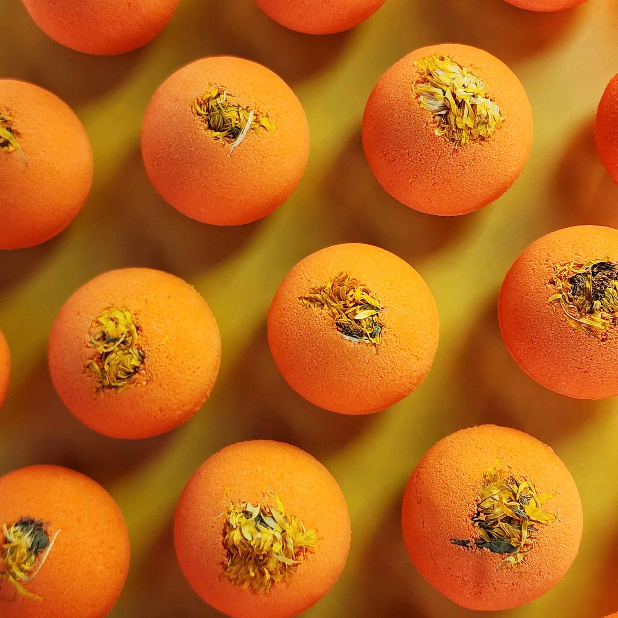 Top-down view of multiple bright orange Restore aromatherapy bath bombs topped with whole dried chrysanthemum flowers