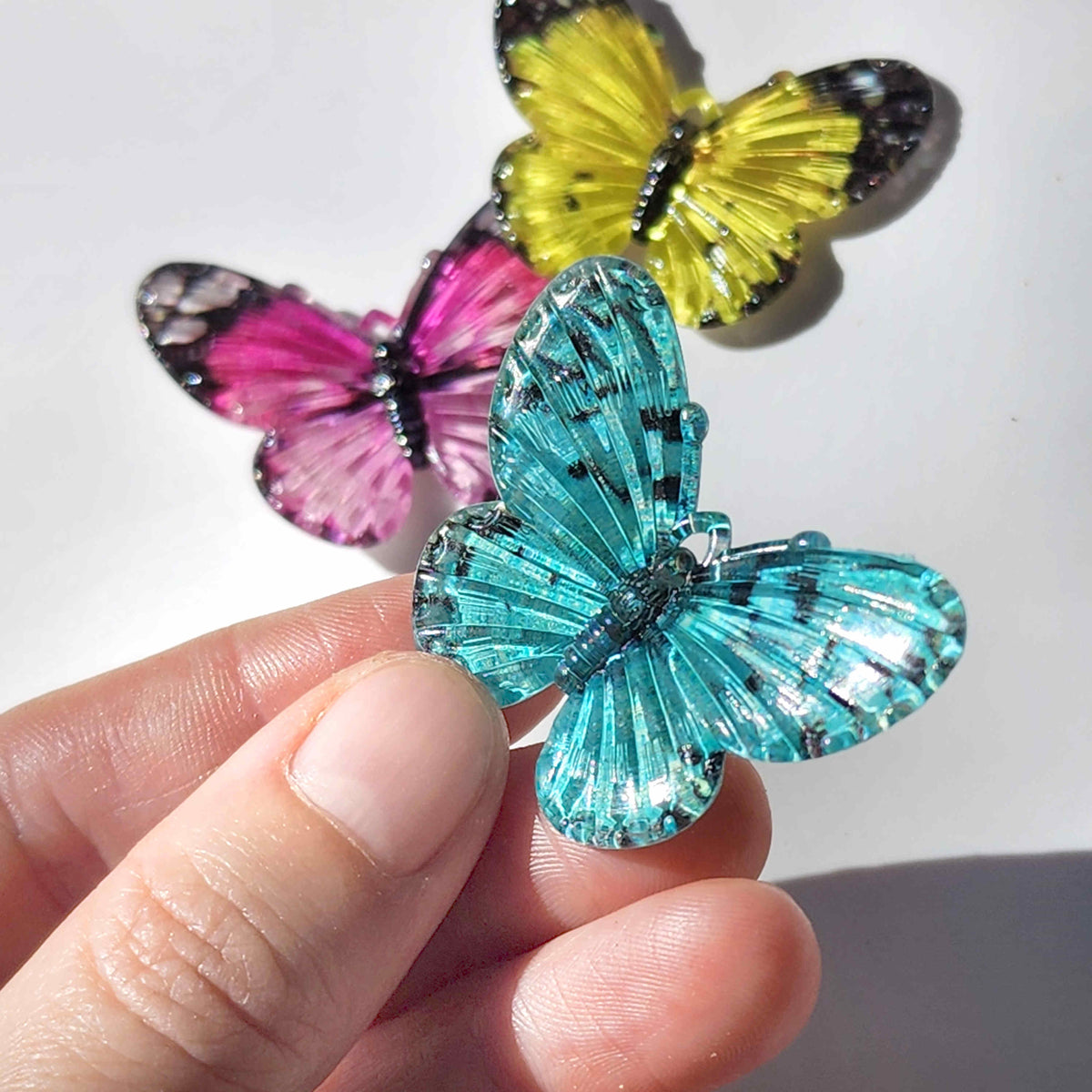 Teal blue acrylic butterfly charm being held between two fingers