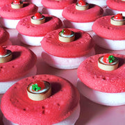 Flat disc shaped bath bombs stacked and placed in a tidy array on a plain pink background