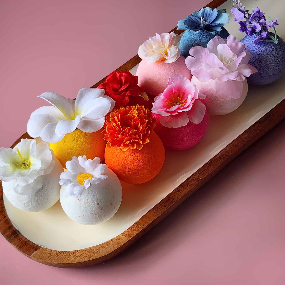 Colorful Botanica Basics bath bombs topped with flowers on a wooden tray