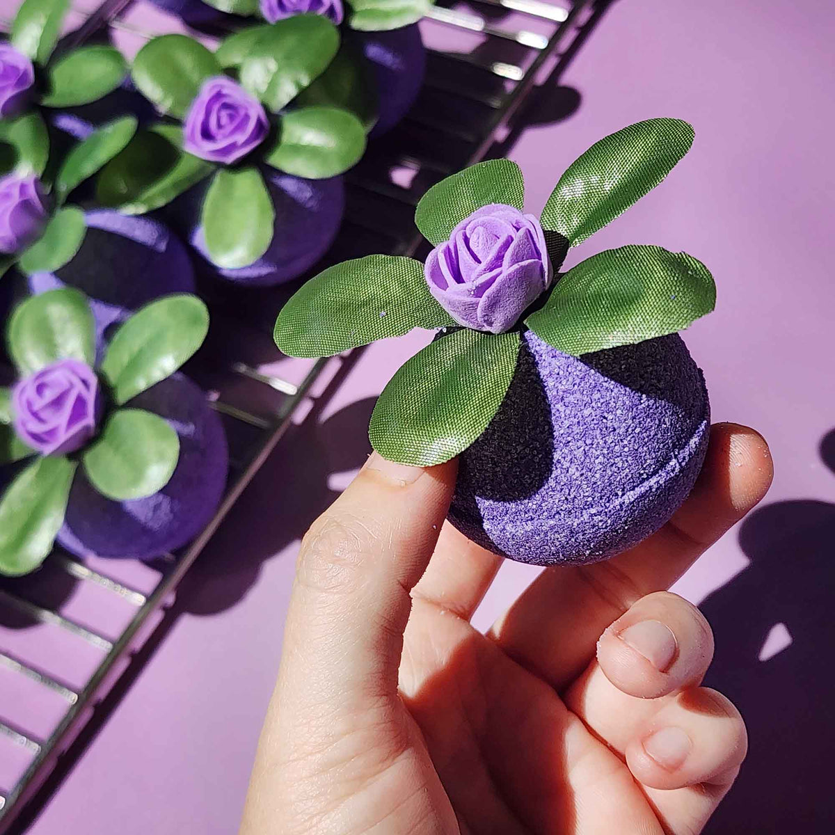 Hand holding the purple Wild Berry bath bomb from the Botanica Basics bundle