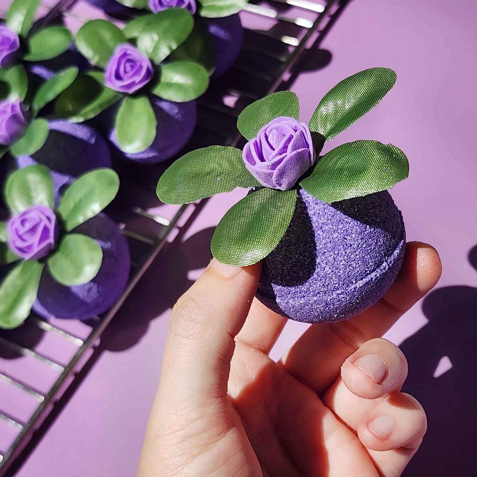 Hand holding a Wild Berry bath bomb in front of a tray of matching bath bombs