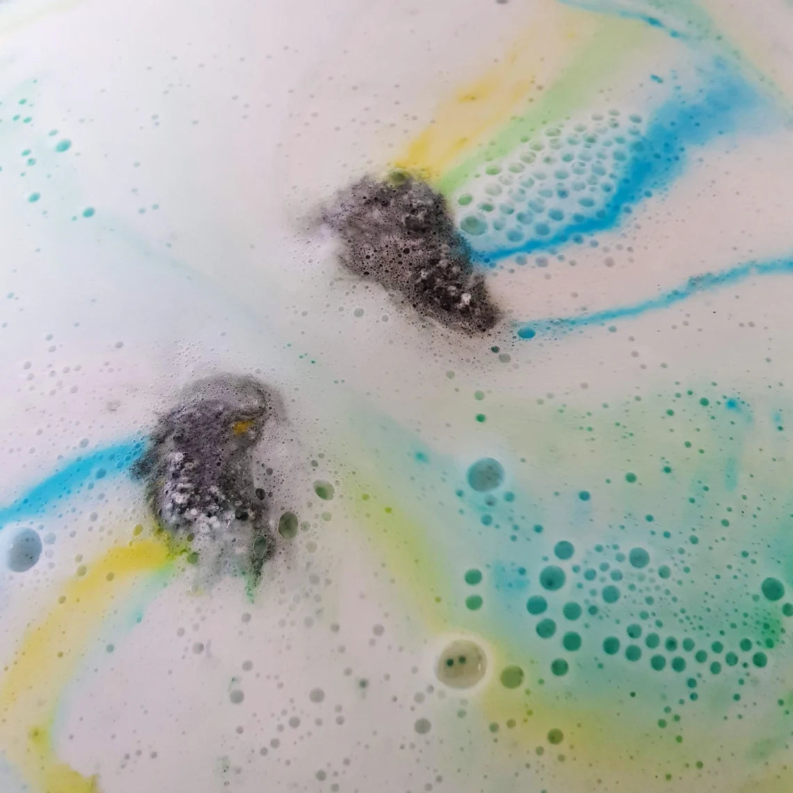 bath bomb foaming and dissolving releasing blue, yellow, and green streaks of colour
