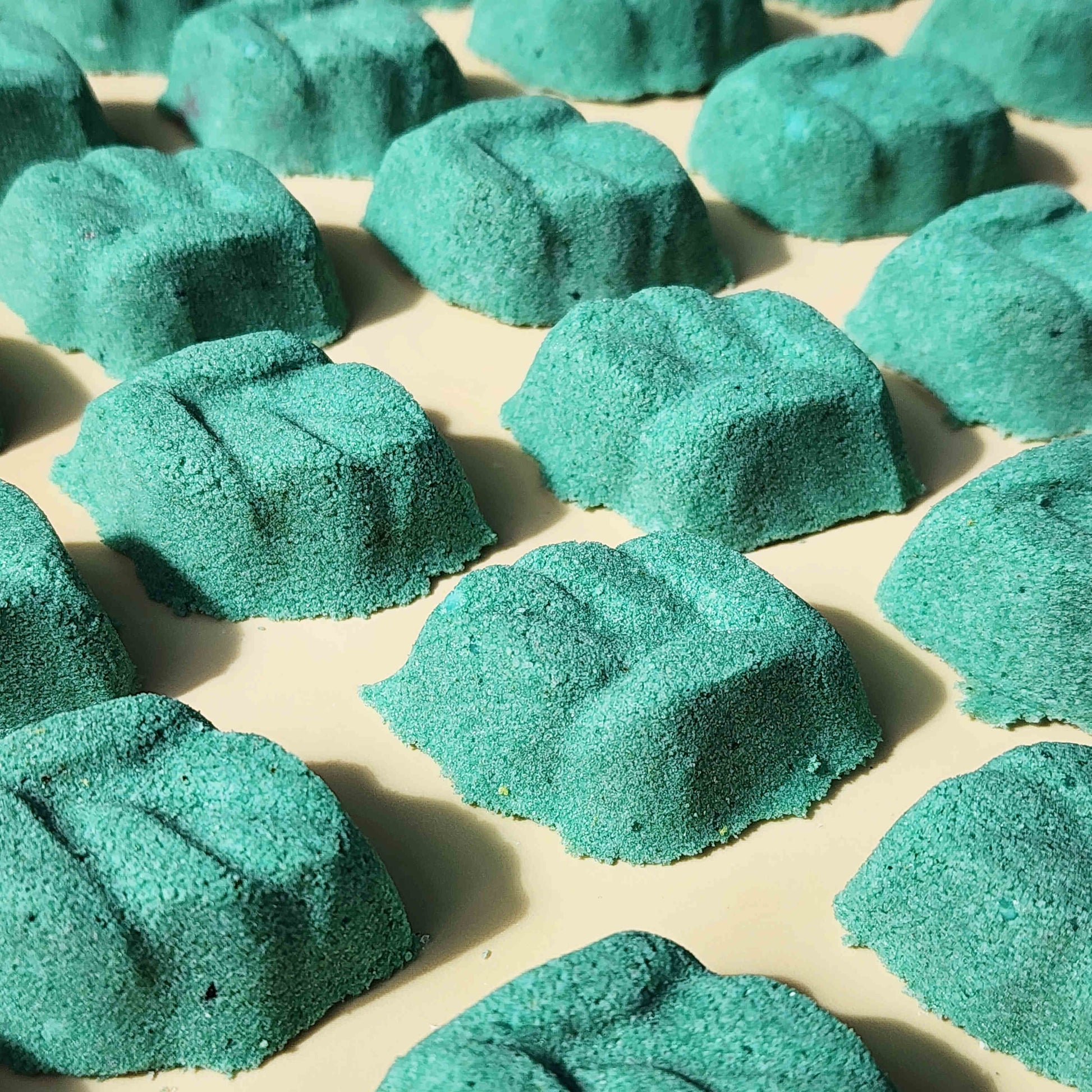 teal leaf shaped mini bath bomb laid out in a neat array over a plain beige background
