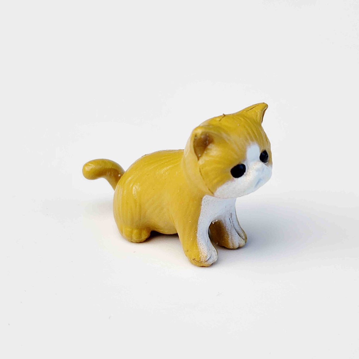 small mustard coloured PVC cat figurine on a white background