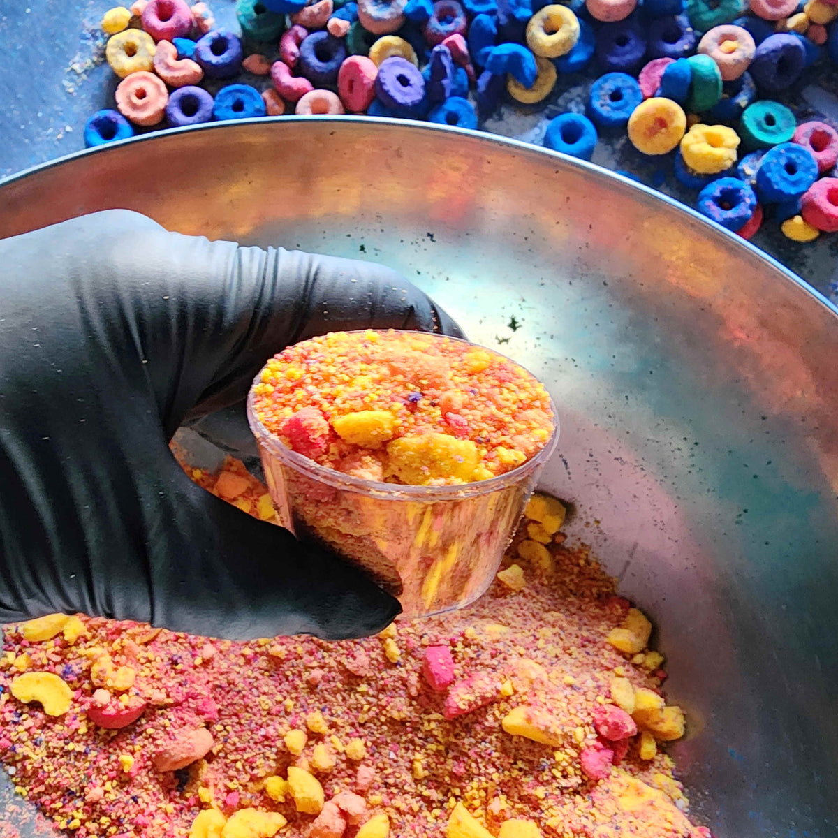 powdered bath bombs in a mixing bowl with fruit loop shaped bath bombs in the background
