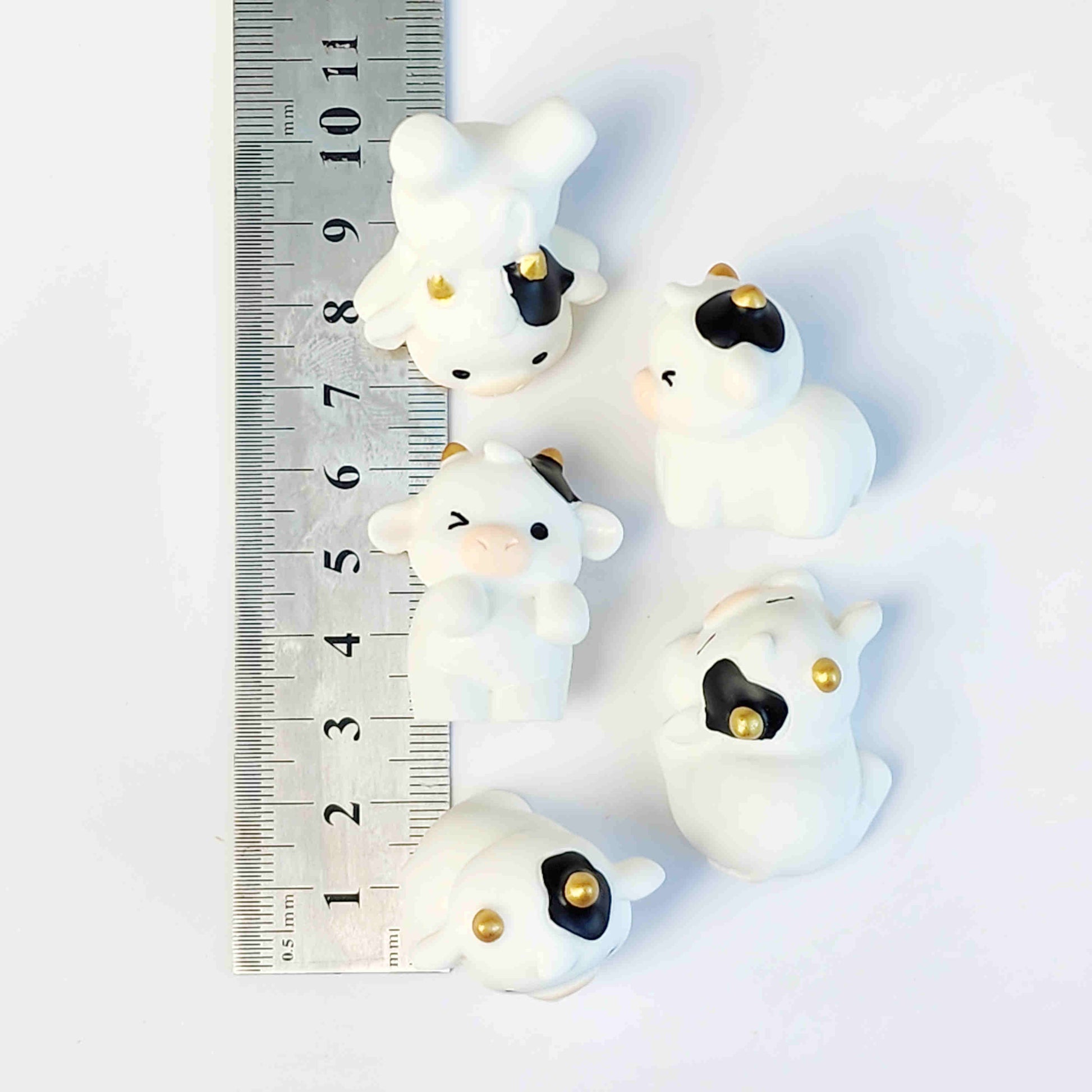 Group of cute cow figurines with gold horns on a white background being measured by a metal ruler
