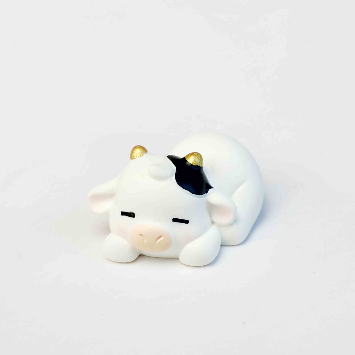 sleeping cute cow figurine with gold horns on a white background
