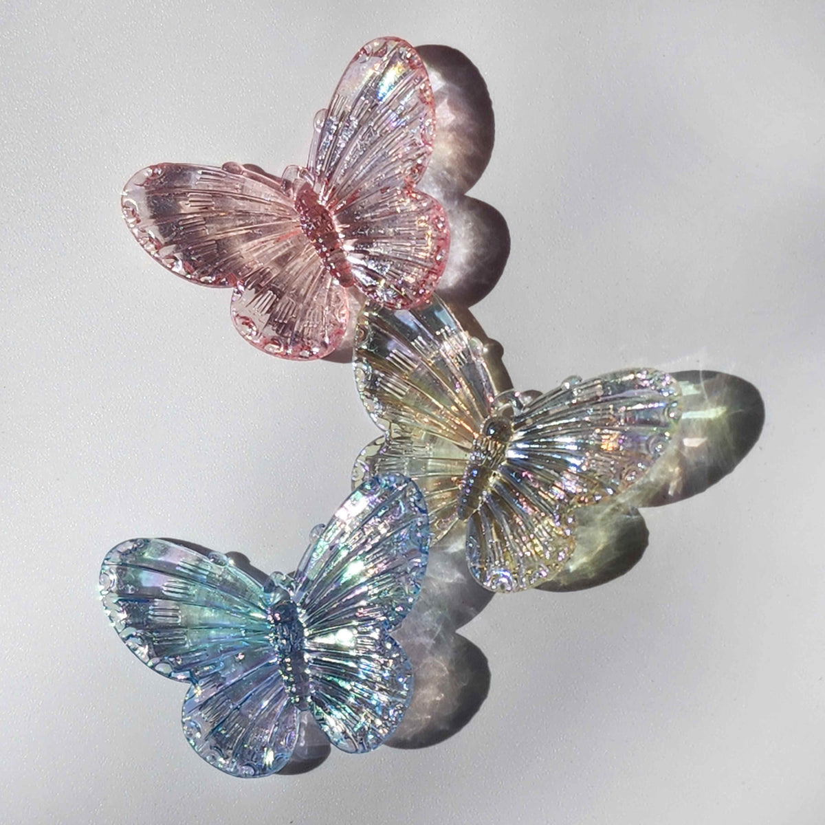 three colour tinted clear butterfly charms refracting light on a white background
