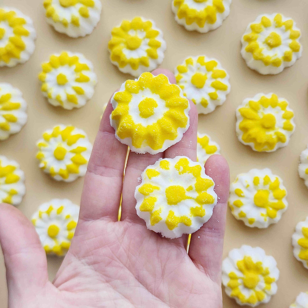 chamomile shaped mini bath bombs with a white base and yellow detail being held in a hand