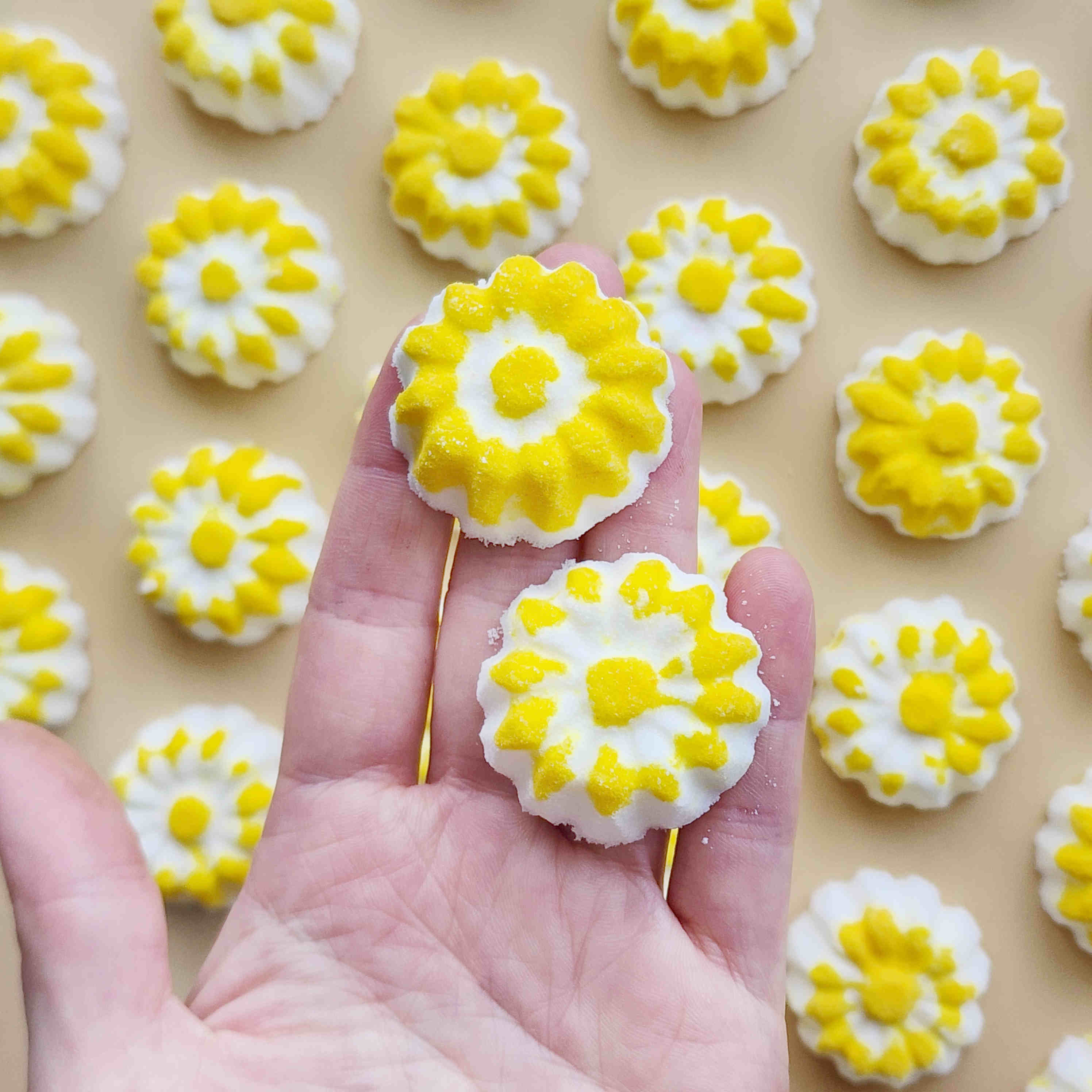chamomile shaped mini bath bombs with a white base and yellow detail being held in a hand
