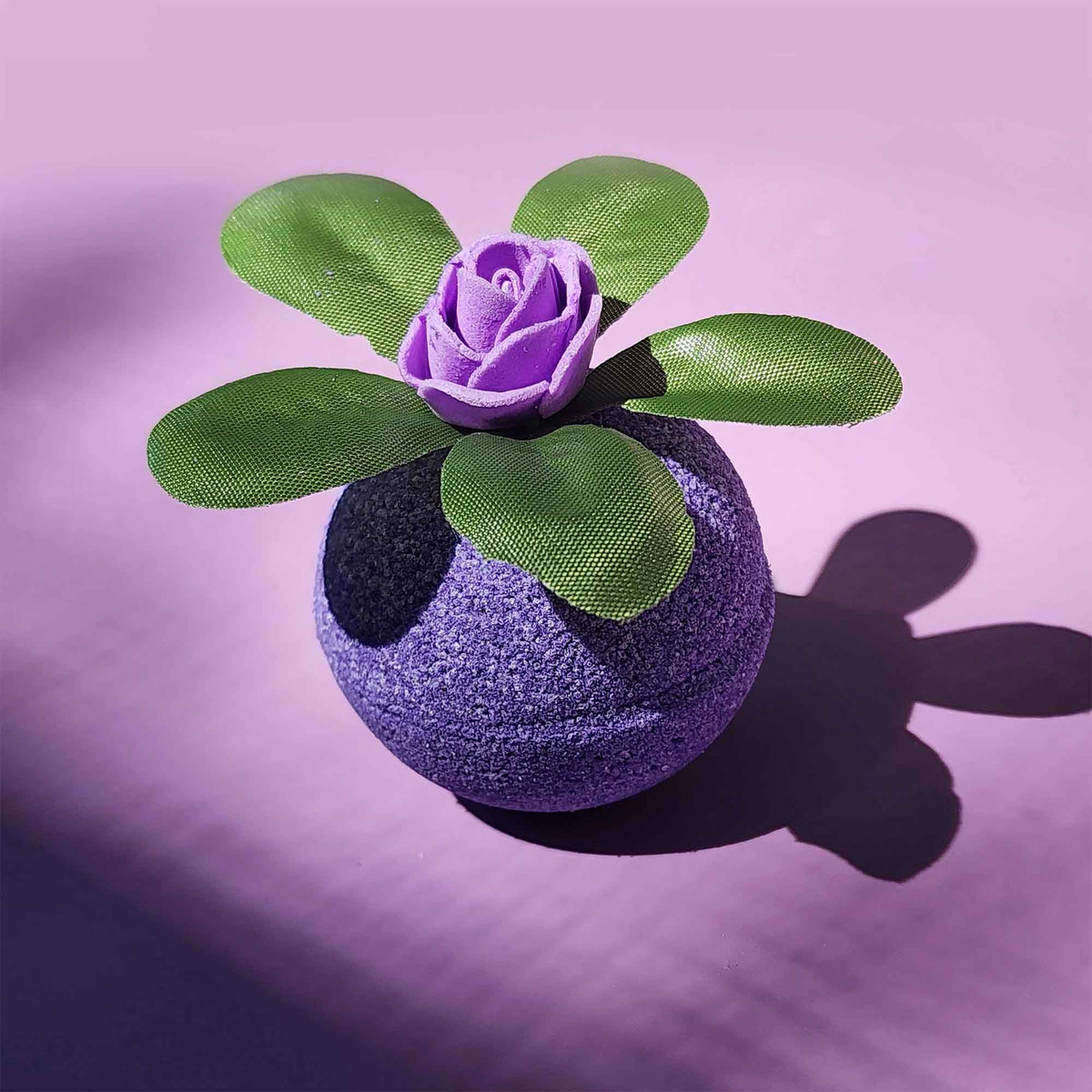 Single purple Wild Berry bath bomb decorated with green leaves and a violet rose