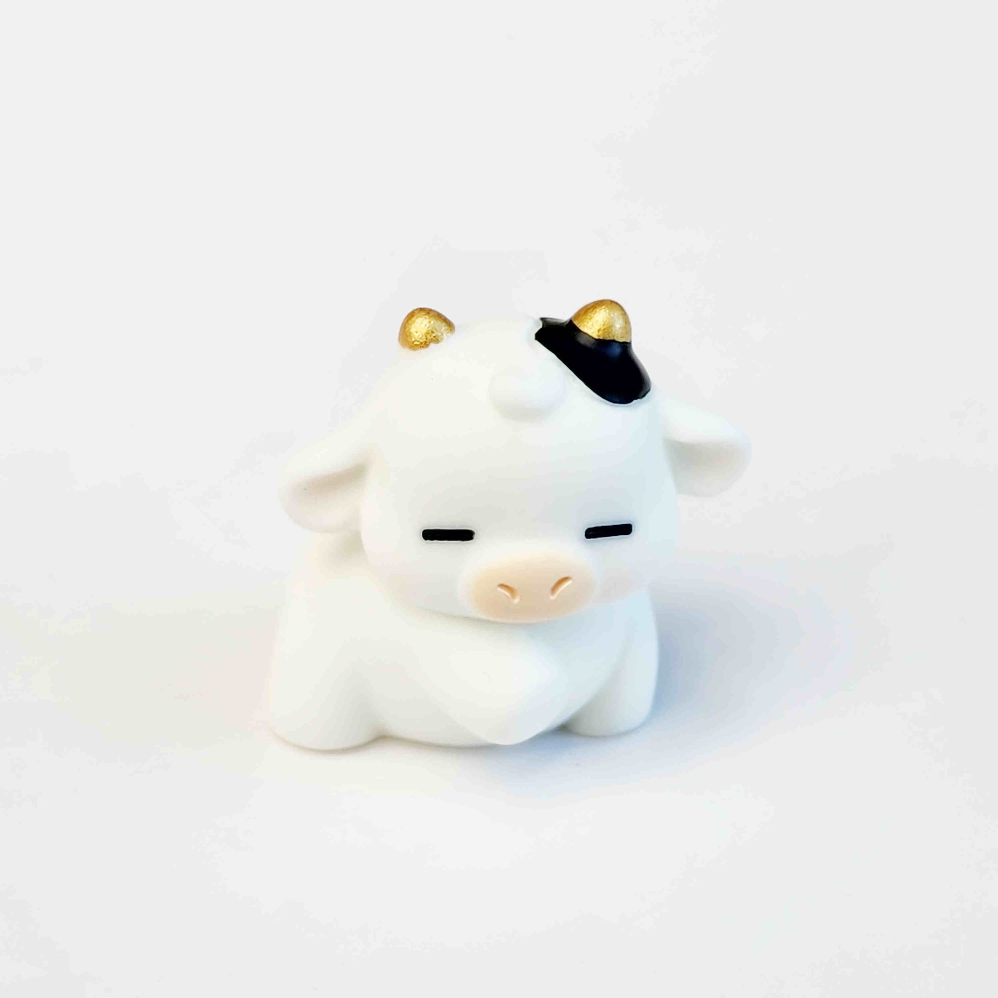 sleepy looking cute cow figurine with gold horns on a white background