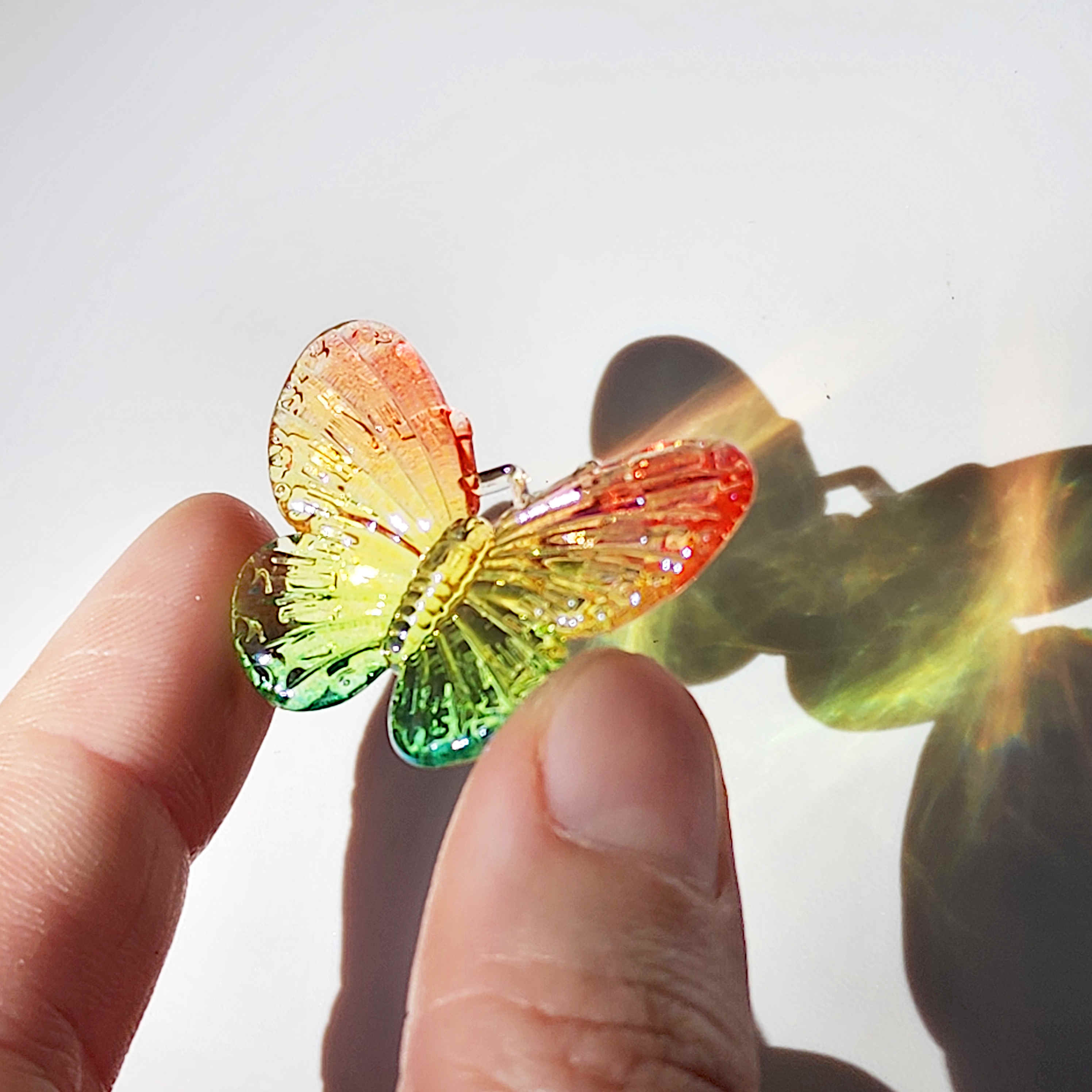 transparent rainbow coloured acrylic butterfly charm being held between two fingers