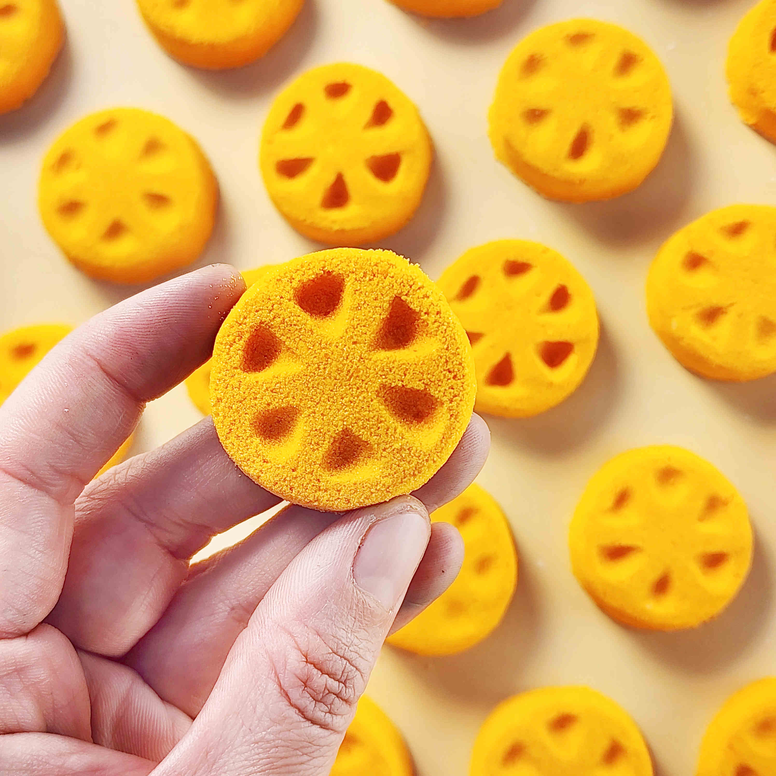 Orange slice shaped mini bath bomb layed out in an array across a plain neutral background