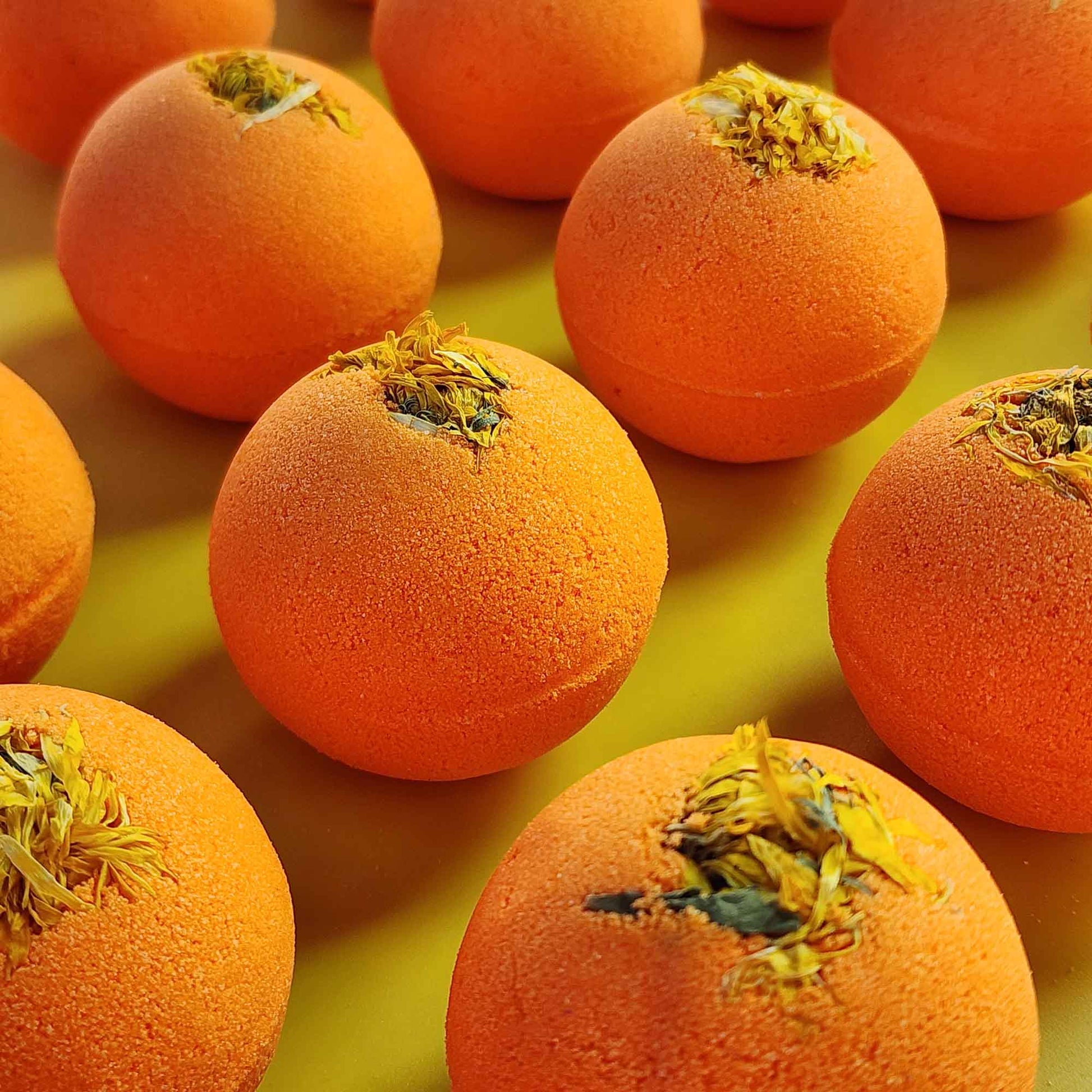 right orange Restore aromatherapy bath bombs topped with whole chrysanthemum flowers on a yellow surface