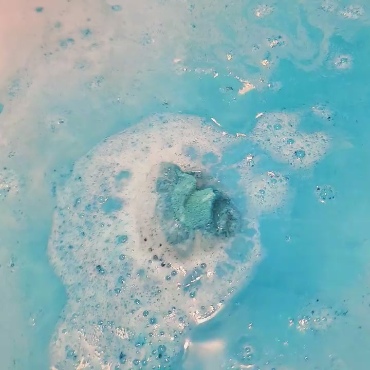 dragon toy partially revealed in a semi dissolved teal bath bomb in bright blue coloured water